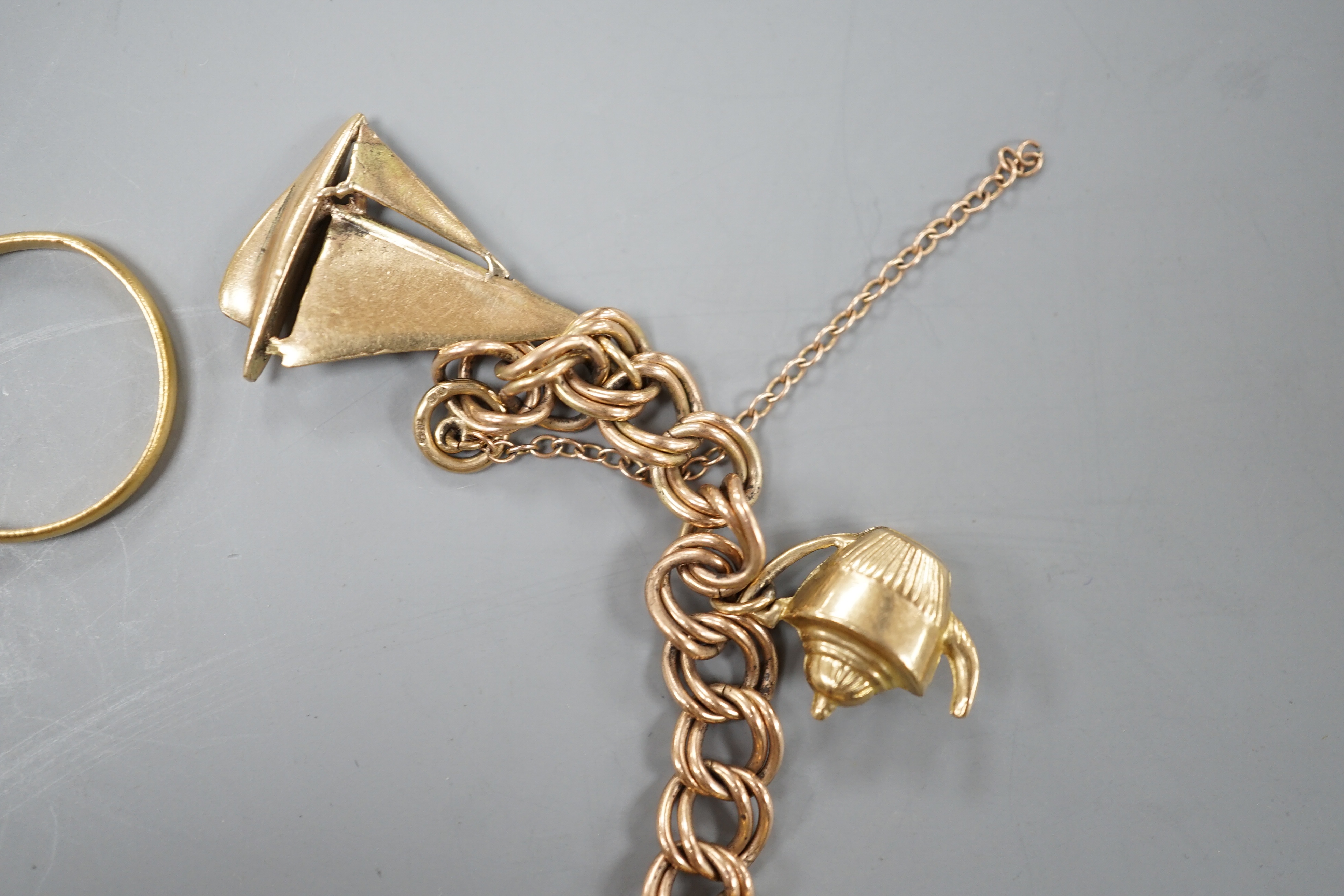 A 1960's 9ct gold charm bracelet, hung with eight assorted mainly 9ct gold charms and a 22ct gold wedding band, gross 28.4 grams.
